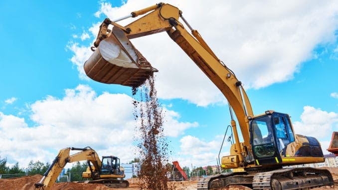 Excavator digging and unloading soil on construction site, highlighting excavation services relevant to project planning.